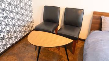 Une chambre d’hôtel avec un lit, deux fauteuils en cuir noir, une table en bois et un mur orné d’un motif.