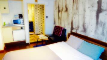 A hotel room with a bed, a desk with a microwave, a chair, and a patterned curtain.
