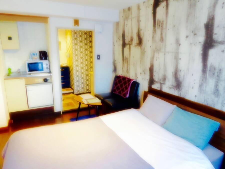 A hotel room with a bed, a desk with a microwave, a chair, and a patterned curtain.
