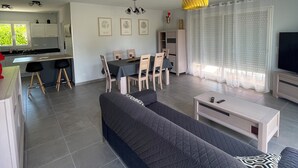 Ein modernes Wohnzimmer mit einem großen Sofa, einem Essbereich mit Stühlen, einer Küche im Hintergrund und einem Fernseher auf einem Schrank.
