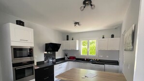 Eine moderne Küche mit weißen Schränken, einer Holztischinsel, zwei schwarzen Barhocker und einem Einbauofen.