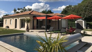 Ein Haus mit Swimmingpool, roten Sonnenschirmen und einem kleinen Schuppen.