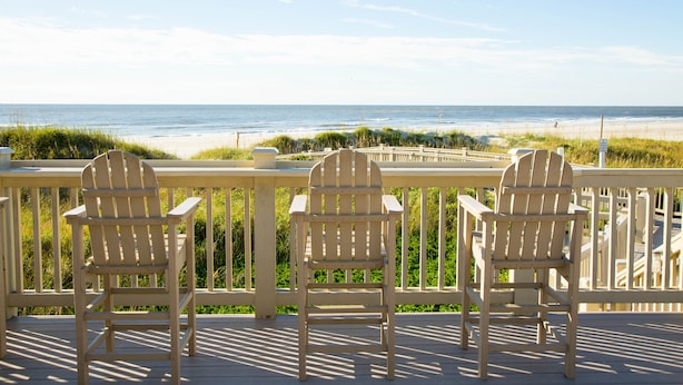 Een houten terras met drie Adirondack-stoelen gericht op het strand.