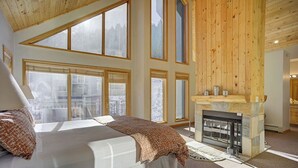 Een slaapkamer met een groot bed, een open haard en meerdere ramen met uitzicht op buiten.
