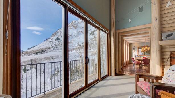 Een ruime kamer met grote schuifdeuren die uitkomen op een balkon met uitzicht op een besneeuwde berg.