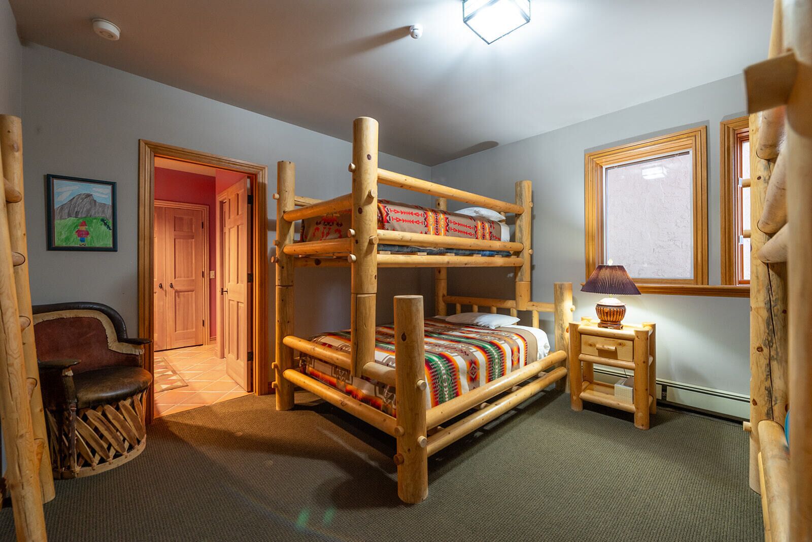 A bunk bed room with a wooden headboard, a small bedside table with a lamp, and a door leading to another room.