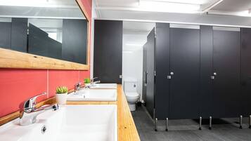 A modern bathroom with a white sink, a mirror, and a toilet. There are black stalls and a red wall.