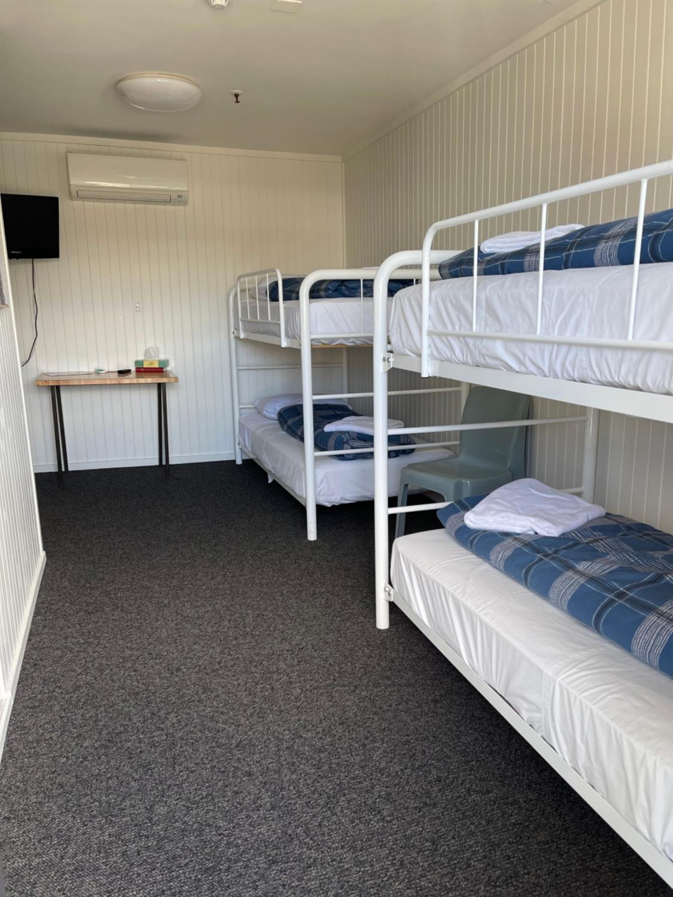 A bunk room with three bunk beds, a small table, and a wall-mounted air conditioner.
