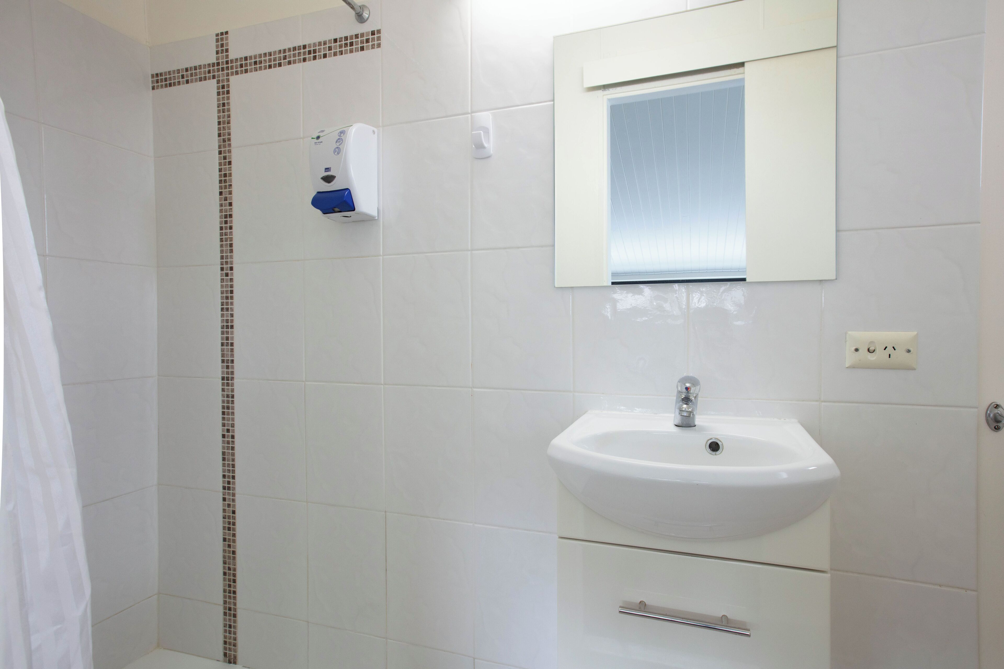 Une salle de bain avec des carreaux blancs, une douche, un lavabo et un miroir.