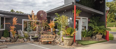 A building with a modern design, featuring a large windmill, a bench, and various potted plants.