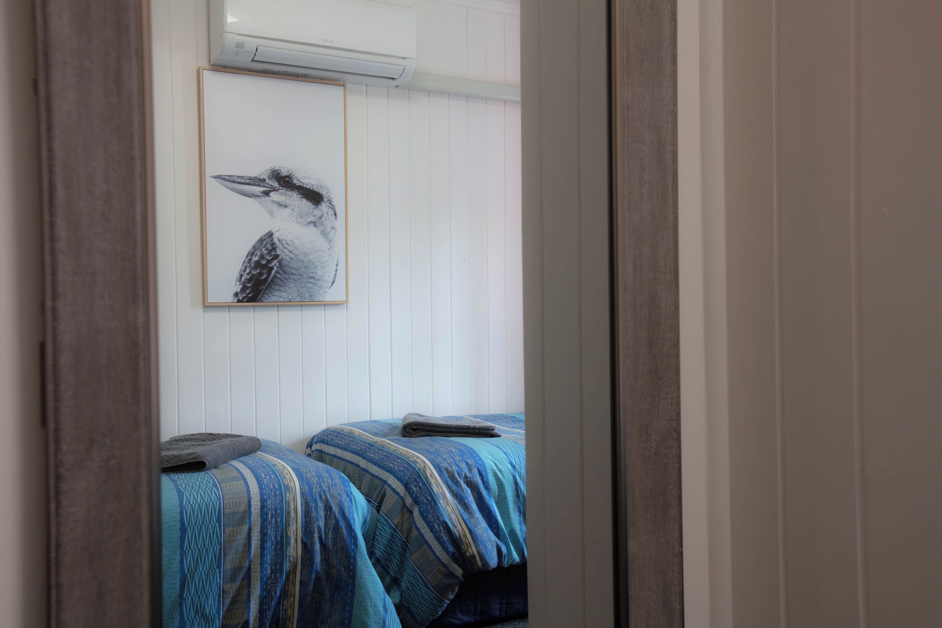 A room with two beds, each with a striped blue and white bedspread. There is a framed picture of a bird on the wall.