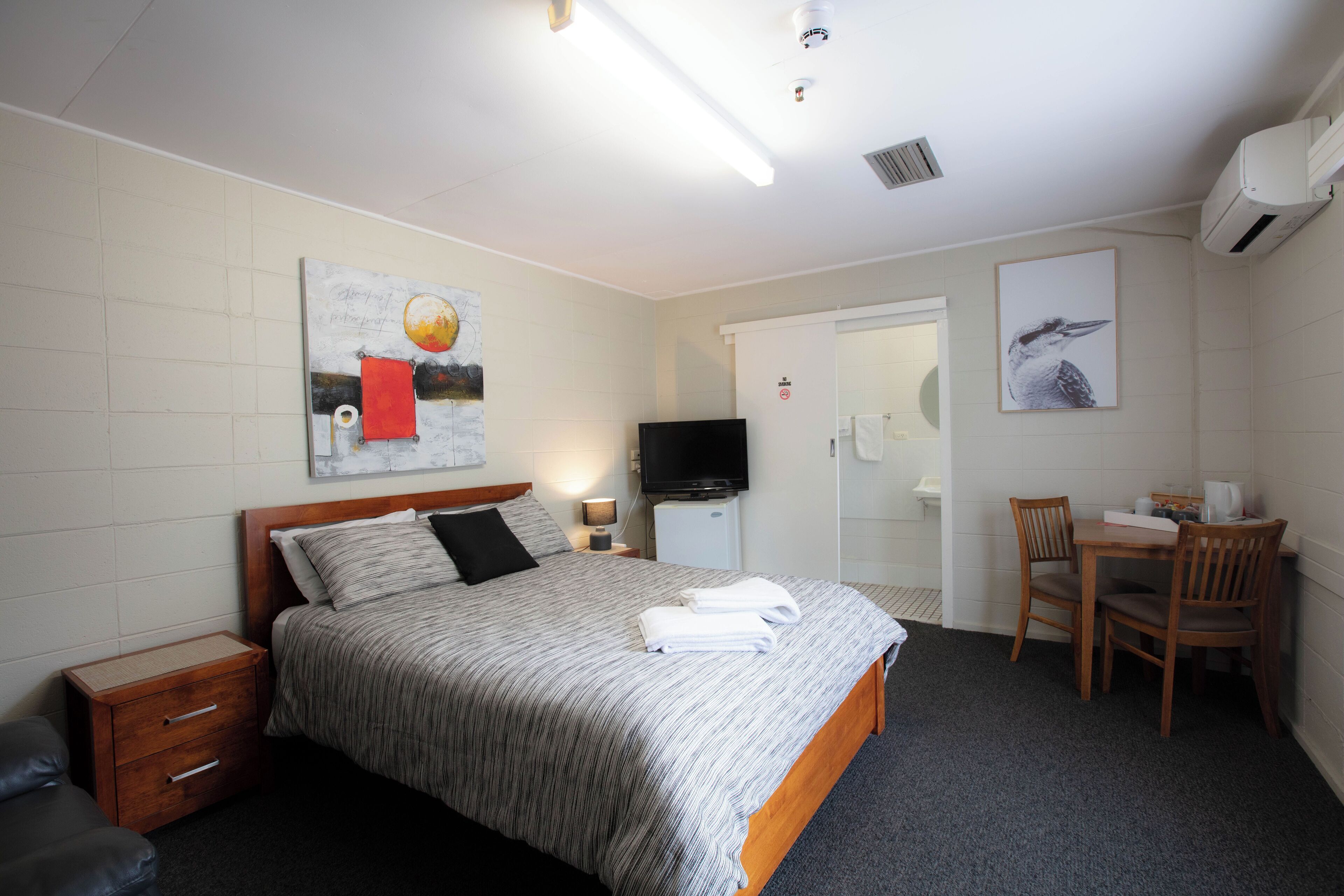 A hotel room with a bed, a desk, a chair, a television, and artwork on the walls.