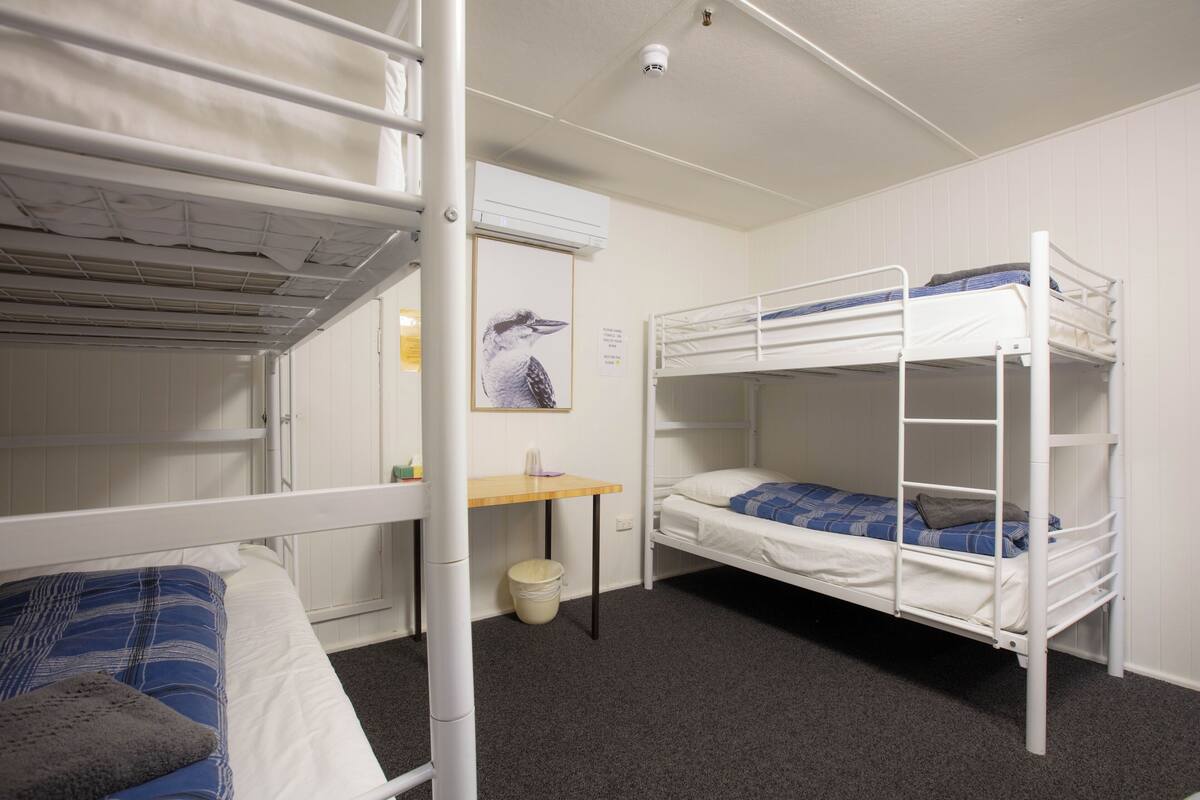 Ein Schlafsaalzimmer mit Etagenbetten, einem kleinen Schreibtisch und einer Wandklimaanlage.