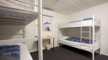 A dormitory room with bunk beds, a small desk, and a wall-mounted air conditioner.