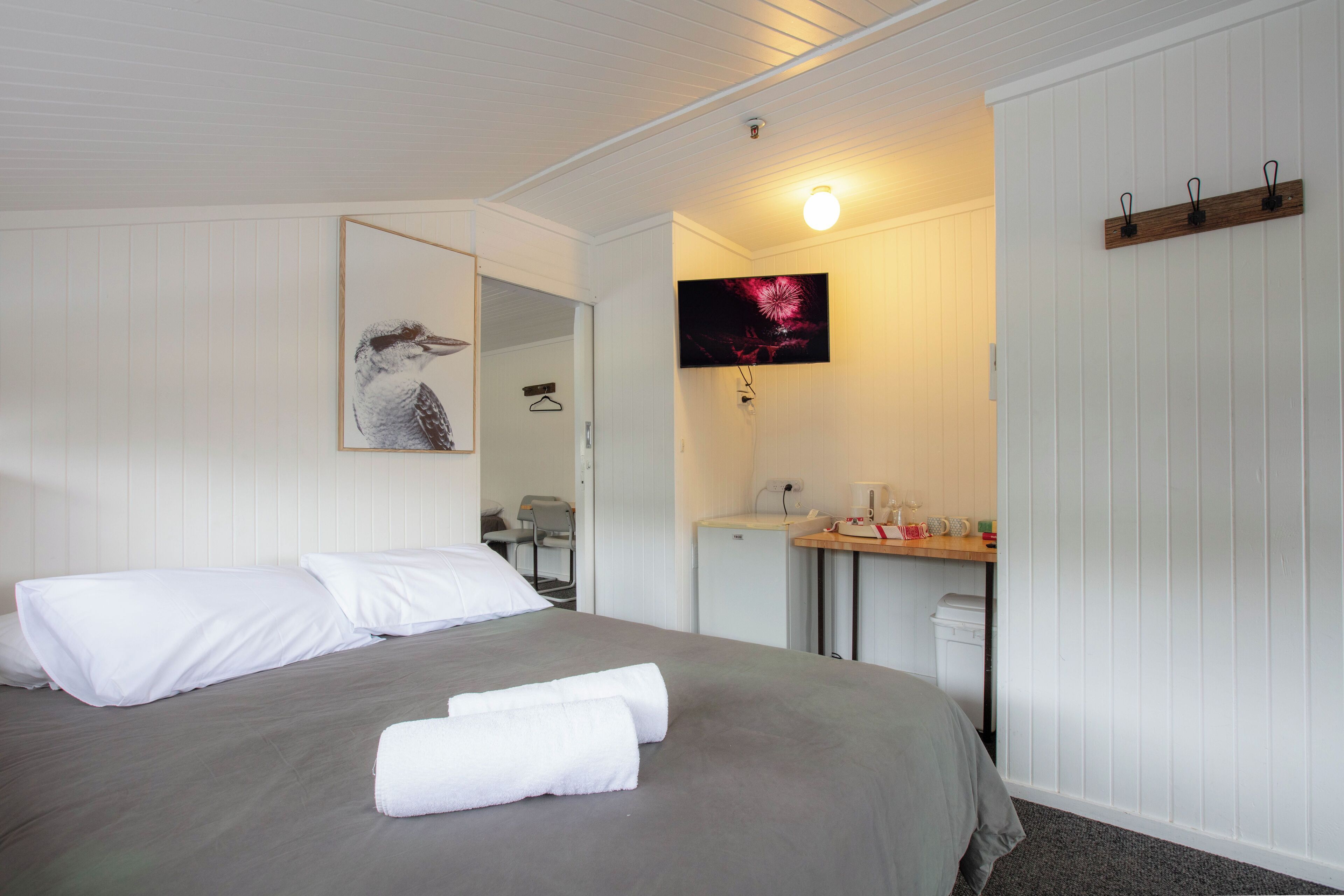 A hotel room with a bed, a desk, a mirror, and a wall-mounted TV.