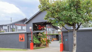 A building with a motorcycle sign, a tree, and a red vehicle inside. - Kookaburra Ski Lodge (Jindabyne)