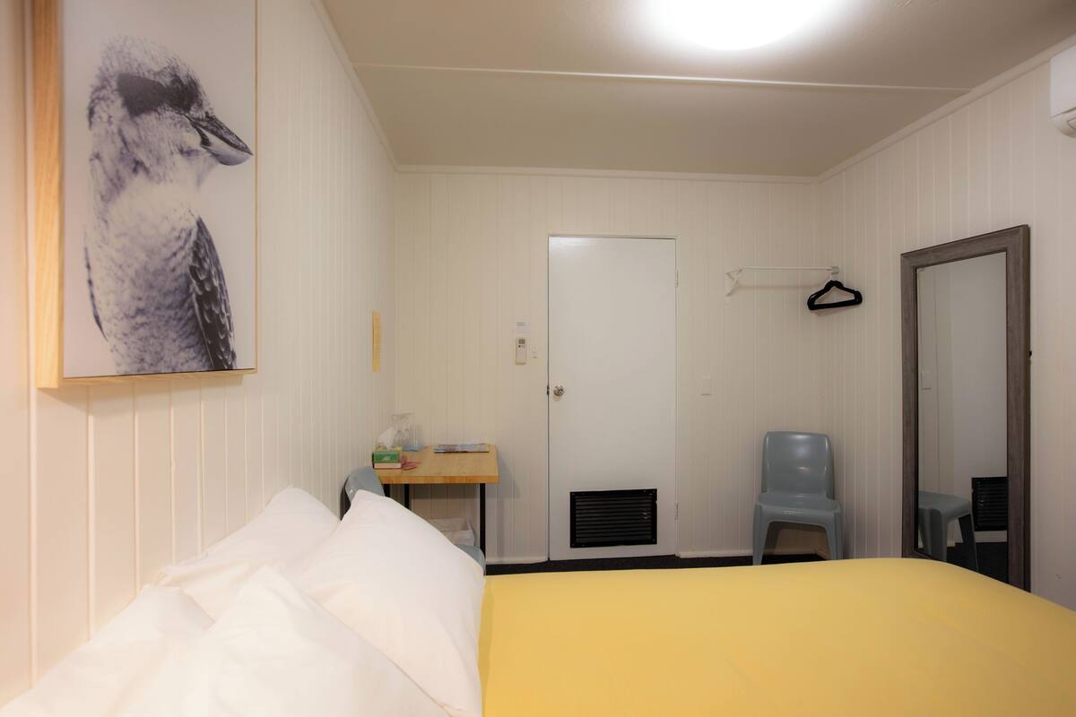 Ein Hotelzimmer mit Bett, Schreibtisch mit Stuhl, Kleiderhaken und einer Tür.