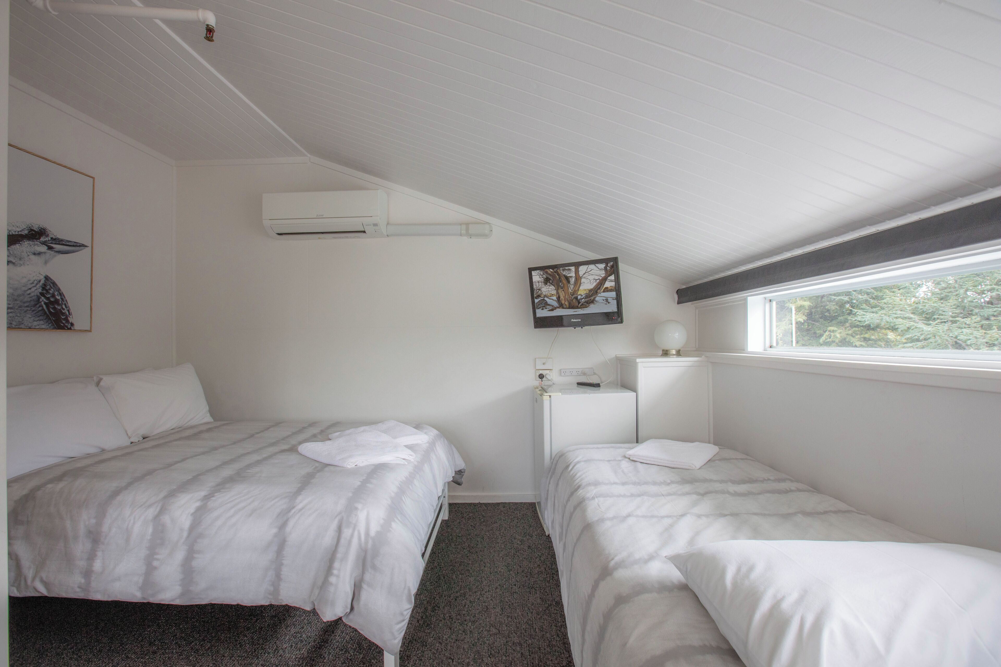 A bedroom with two beds, a window, and a wall-mounted TV.
