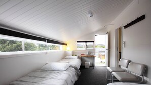 A room with three single beds, a desk with a chair, a small table, and a window with a view of trees and mountains. - Kookaburra Ski Lodge (Jindabyne)
