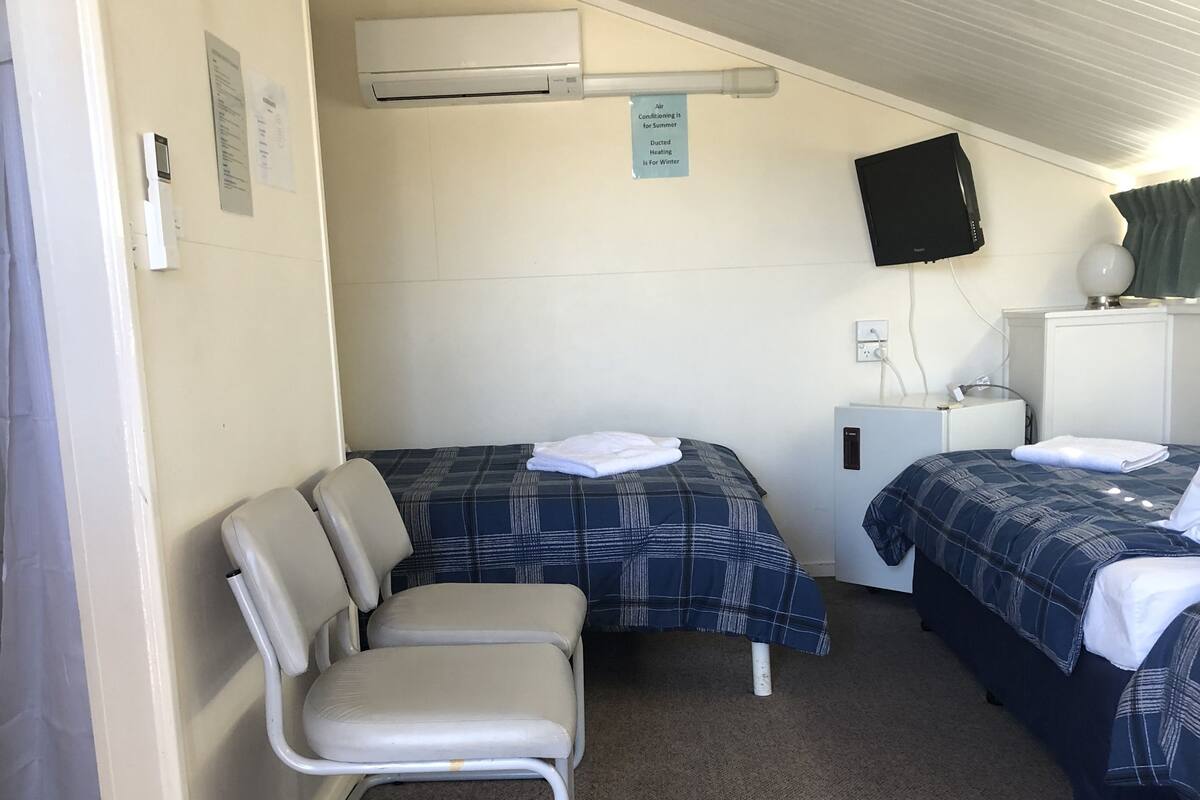 Ein kleines, kompaktes Zimmer mit zwei Betten, einem Sessel, einem Schreibtisch und einem Fernseher.