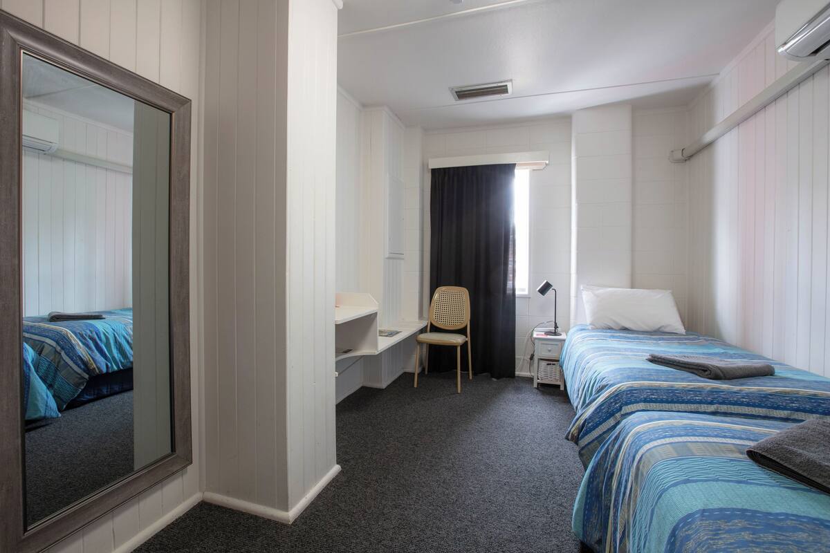 Ein Hotelzimmer mit zwei Betten, einem Schreibtisch, einem Stuhl und einem großen Spiegel.
