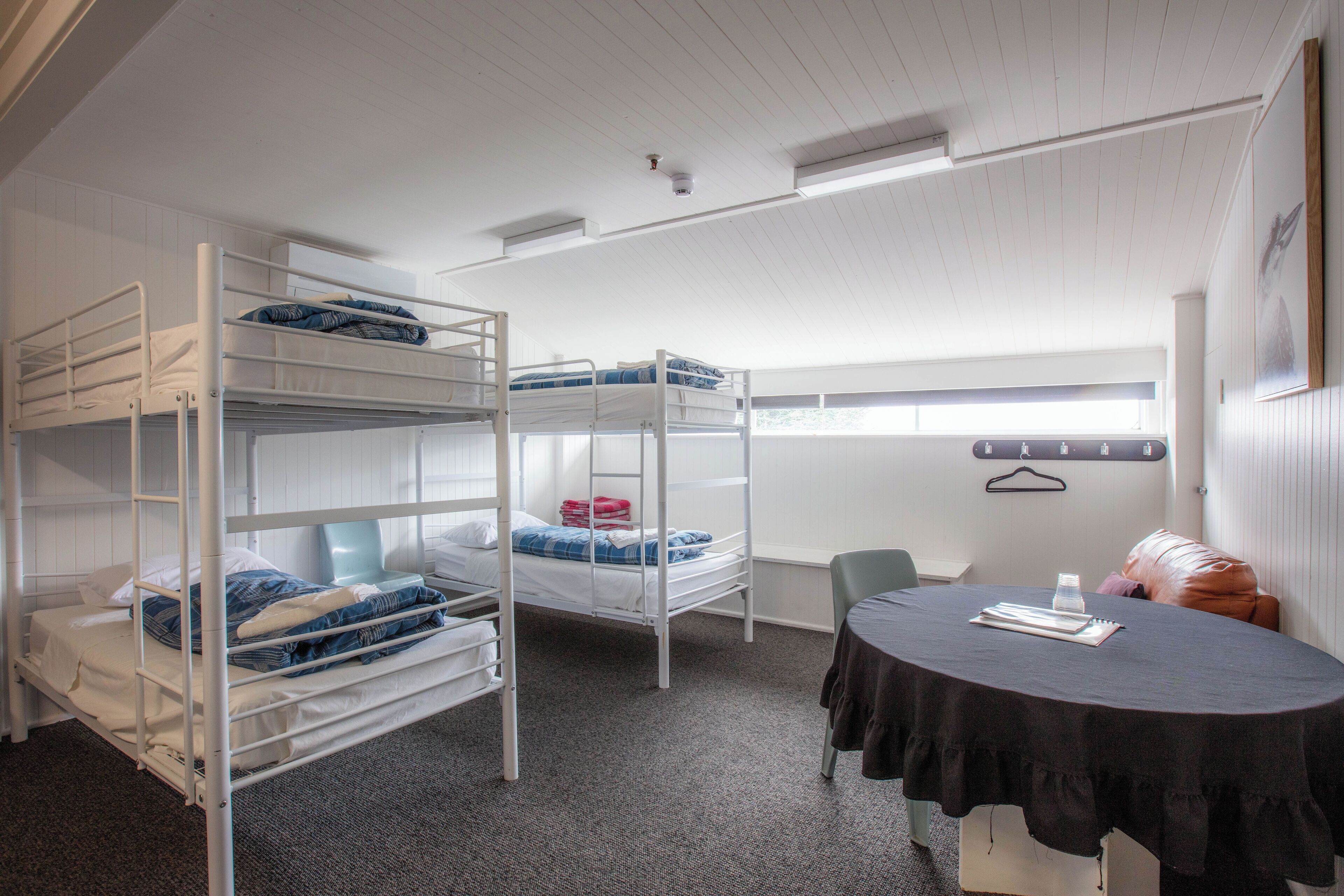 A dormitory room with bunk beds, a table with a black tablecloth, and a chair.