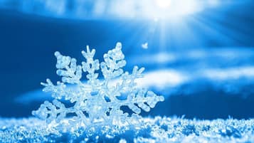 Um floco de neve sobre uma superfície com fundo azul e luz solar.