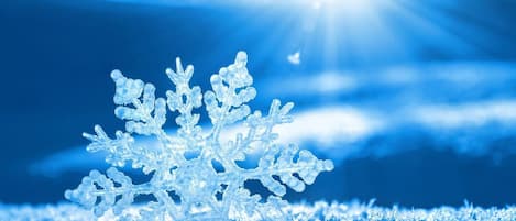 A snowflake on a surface with a blue background and sunlight.
