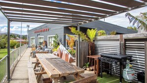 An outdoor patio with picnic tables, a barbecue grill, and a covered area with a metal roof. - Kookaburra Ski Lodge (Jindabyne)
