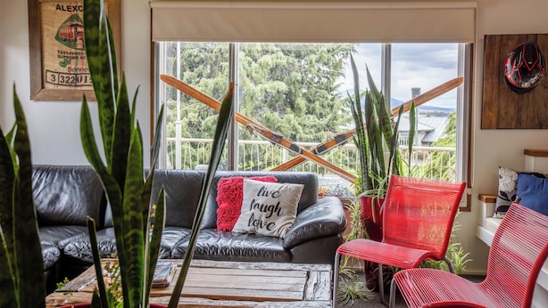 A cozy living room with a leather sofa, a red chair, and a coffee table. There is a window with a view of trees and a building. - Kookaburra Ski Lodge (Jindabyne)