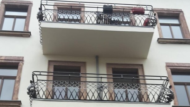 Un edificio de varios pisos con balcones, cada uno con barandillas de metal y macetas con plantas.