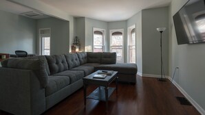 Una sala de estar con un sofá modular, una mesa de centro y un televisor de pantalla plana montado en la pared.