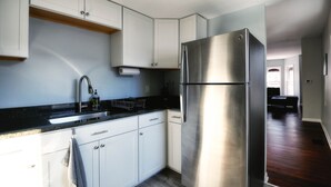 Una cocina moderna con armarios blancos, un refrigerador de acero inoxidable y una encimera negra.
