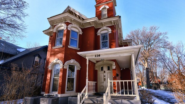 Una casa de ladrillo rojo de estilo victoriano con un porche y escalones blancos, número 116.