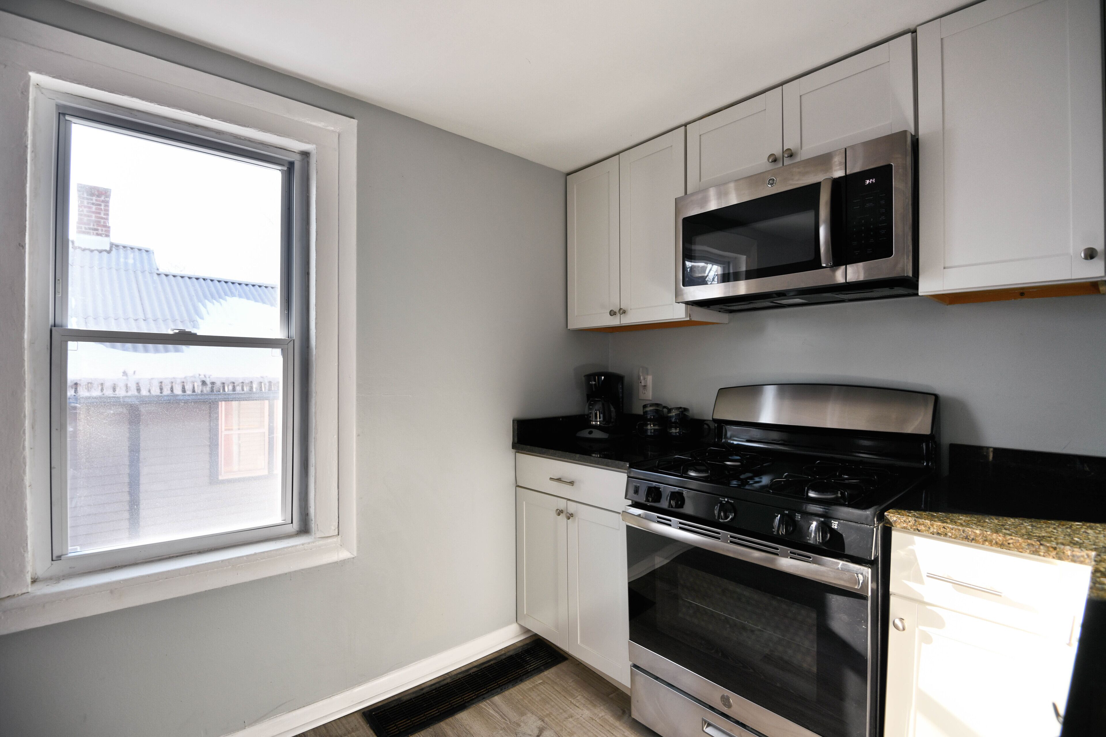 A kitchen with white cabinets, a black stove, a microwave, and a window with a view of buildings outside.