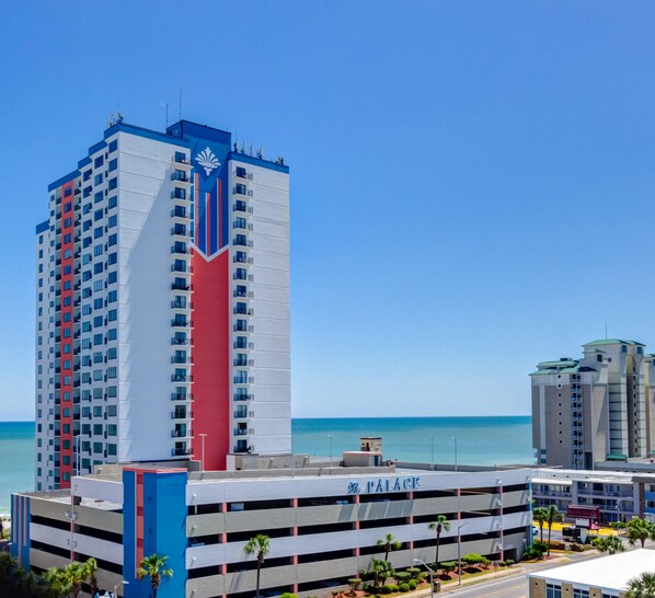 Un grand hôtel à la façade rouge et bleue remarquable, doté d’un parking et offrant une vue sur l’océan.