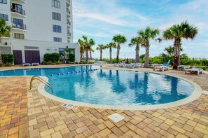 Une piscine entourée d’une terrasse en briques, de palmiers et de chaises longues.