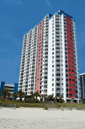 Un hôtel de grande hauteur doté de nombreux balcons, situé près d’une plage de sable.