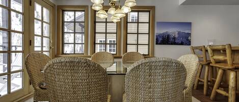 A dining area with a round table, wicker chairs, and a chandelier.