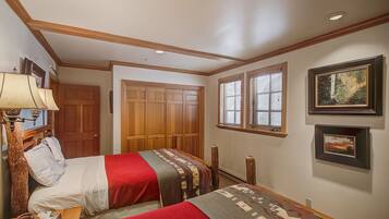 A hotel room with two beds, wooden wardrobe, framed pictures on the wall, and a window with blinds.