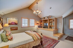 A bedroom with a bed, a chandelier, a shelf with decorative items, and a window with blinds.