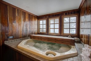 A wooden-paneled bathroom with a freestanding bathtub, a window, and a control panel.
