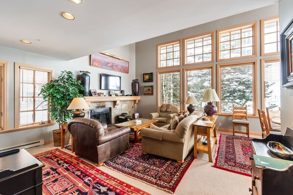 A spacious living room with a fireplace, large windows, and a variety of seating options.