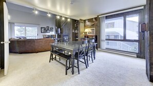 A spacious living room with a large dining table, a fireplace, and a view of the outside.