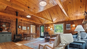 A cozy cabin interior with wooden walls, a fireplace, a dining area, and a comfortable seating space.