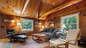 A cozy cabin interior with wooden walls, a leather chair, a sofa, a small table, and a rug.