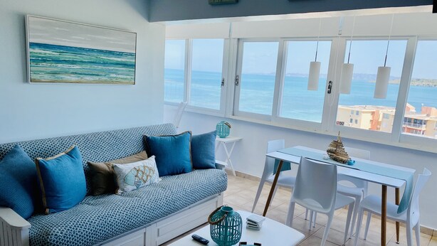 Olohuoneessa on sohva, sohvapöytä ja ruokapöytä, suuret ikkunat, joista on näkymä merelle, sekä seinällä taulu.