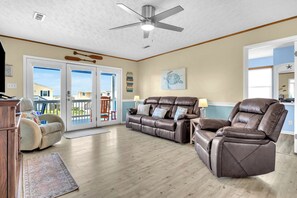 A spacious living room with a brown leather sofa, a recliner, and a ceiling fan.