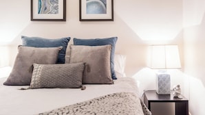 Une chambre à coucher avec un lit, des oreillers, une table de chevet avec une lampe, et deux œuvres d’art encadrées accrochées au mur.