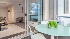 Un espace de bureau moderne avec une cloison en verre, une table ronde en verre agrémentée d’une plante, des chaises blanches et un canapé gris.